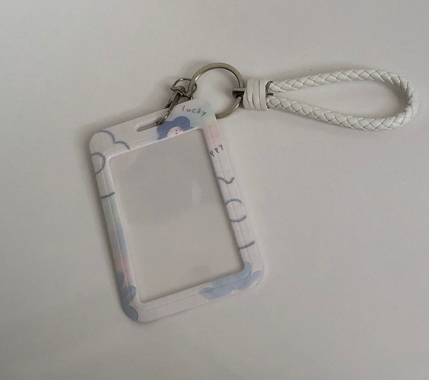 White Id holder with light purple flower patterns. Lucky and happy written in different places. Silver key ring with a white strap attached to it.